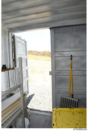 This is a photograph of an interior storage or utility space, likely at one of Epstein's properties. The image shows an open doorway leading to an outdoor area with gravel and landscaping. Inside, there are shelving units, storage containers, cleanin