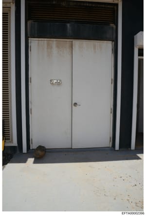 This is an evidence photograph showing a double-door entrance with a visible 'No Smoking' sign mounted on the doors. The doors appear worn with stains and discoloration on their surfaces. The image documents the exterior condition of what appears to 