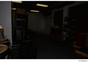 This is a photograph of a kitchen interior, likely taken as evidence documentation during the investigation. The image shows a galley-style kitchen with appliances, countertops, and storage shelving. The photo appears underexposed or taken in low lig