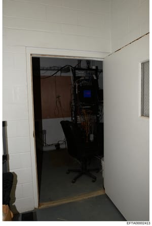 This photograph shows an interior room or closet space containing computer equipment, networking infrastructure, and various cables. The image appears to be from a property search or evidence documentation, showing a workspace with a desk chair, elec