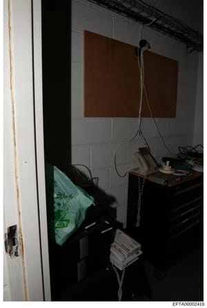 This is a photograph of an interior room space containing various electronic equipment and furnishings. The image shows a desk or work surface with multiple items including what appears to be communication or monitoring equipment, with cables and wir