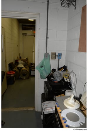 This is an evidence photograph depicting a utility or storage room with white tile walls, yellow painted doors, and various maintenance equipment and supplies. The room contains HVAC equipment, electrical boxes, coiled cables, storage boxes, and bath