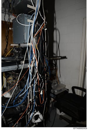 This photograph documents computer server equipment, networking hardware, and cabling infrastructure in what appears to be a utility or server room. The image shows stacked servers, patch panels, power supplies, and extensive network cabling in vario