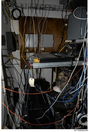 This photograph shows an interior view of a computer server room or technical installation space containing multiple networking and server equipment with extensive cable management. The image documents various hardware components including servers, n