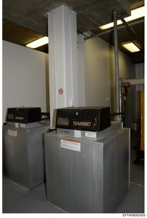 This is a photograph of industrial HVAC equipment (two Tramont units) installed in what appears to be a basement or mechanical room of a property. The image shows commercial heating/cooling infrastructure with a tall white vertical duct or chimney, m