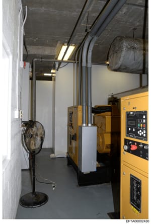This photograph depicts an industrial utility or mechanical room, likely part of a property under investigation. The space contains multiple pieces of heavy equipment including generators (yellow Caterpillar units), HVAC systems, ductwork, and a port