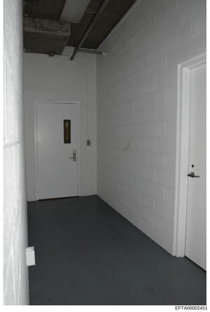 This is an evidence photograph showing an interior hallway or basement corridor with white cinderblock walls, a dark floor, and multiple white doors. The image appears to be from a property inspection or evidence documentation, likely from one of Eps