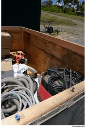 This photograph shows the interior of a wooden trailer or storage container filled with various equipment and supplies including coiled hoses, electrical cords, tools, boxes, and other maintenance equipment. The image appears to be evidence documenta