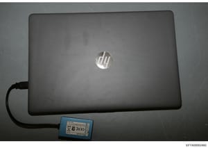 This is a photograph of a gray HP laptop computer with an attached external hard drive or memory device (blue unit with visible label). The image appears to be evidence documentation from the investigation, with a Bates stamp indicating it was catalo