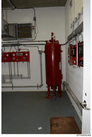 This photograph documents the interior of a mechanical equipment room, featuring fire suppression and HVAC systems including a large red pressurized tank, control panels, ducting, and electrical fixtures. The image appears to be evidence documentatio