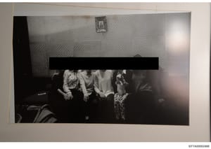 This is a black and white photograph showing four individuals seated together on what appears to be a dark sofa or couch in an interior room with textured wallpaper. A significant portion of the photograph has been redacted with a black bar obscuring