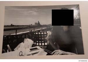 This is a black and white photograph showing a person dining at an outdoor restaurant or terrace overlooking the Grand Canal in Venice, Italy. The image captures a scenic waterfront setting with the Basilica di Santa Maria della Salute visible in the