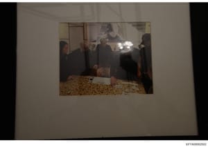 This is an evidence photograph showing five people standing in what appears to be a residential interior space with distinctive patterned flooring. The image quality is somewhat compromised by glare and the angle of the photograph. The context and id