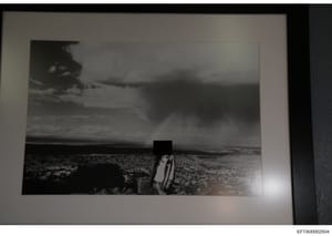 This is a black and white photograph showing a desert landscape with sparse vegetation. A human figure in the center of the image has been redacted with a black box obscuring their identity. The photo appears to be evidence documentation from the inv