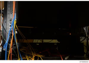 This is a photograph of electrical/networking equipment showing a server rack or panel with multiple colored wires (blue, orange, yellow, red, green) connected to numbered ports. The image appears to be documentation of infrastructure or equipment se