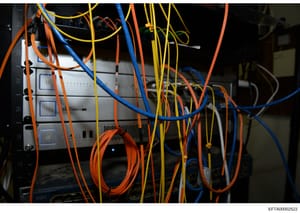 This is a photograph of server or network equipment showing multiple colored ethernet and power cables connected to a rack-mounted device with multiple port connections. The image appears to be evidence documentation related to digital infrastructure