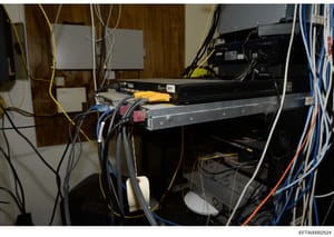 This photograph documents a server room or network equipment installation, showing various electronic components including servers, networking devices, and extensive cabling infrastructure. The image captures the technical setup of what appears to be