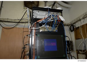 This is an evidence photograph showing a computer network infrastructure setup with multiple server units, network switches, and extensive cabling in various colors (orange, blue, white, black). The equipment appears to be mounted in a rack with a mo