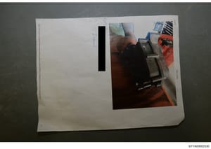This is an evidence photograph showing a close-up view of what appears to be a mechanical device or component being held in someone's hand. A significant portion of the photograph is redacted with black bars, obscuring identifying information. The im