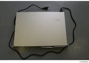 This is a photograph of a light box or similar illumination device with attached black power cables, documented as physical evidence in the Epstein investigation. The device appears to be a flat, white panel with electrical connections, photographed 