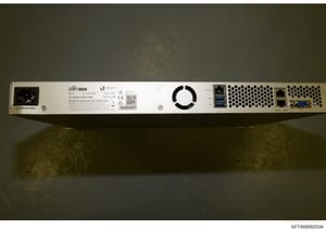 This is a photograph of the rear panel of a Ubiquiti UniFi network device, showing power connections, cooling fan, network ports, and FCC compliance information. The device appears to be server or networking equipment seized as evidence in the invest