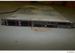 This is a photograph of a hewlett-Packard rack-mounted server unit with multiple hard drive bays, taken as evidence documentation. The device shows visible wear and dust accumulation, suggesting it was seized from an operational environment. The phot