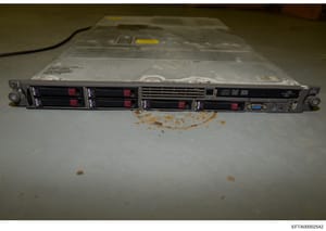 This photograph depicts a rack-mounted server unit (appears to be an HP ProLiant or similar enterprise server) with four hot-swappable hard drive bays containing red hard drives, captured as physical evidence during the investigation. The device show