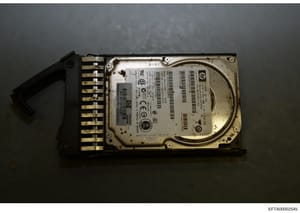This is a forensic evidence photograph of a computer hard drive with an attached connector bracket. The drive bears visible serial numbers and identification markings, suggesting it was seized as physical evidence. The label includes HP/Compaq brandi