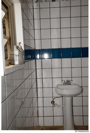 This is an evidence photograph of a bathroom interior, showing a pedestal sink, white subway tile walls with a blue accent stripe, and bathroom fixtures including a GOJO soap dispenser. The image documents the condition and layout of a bathroom space