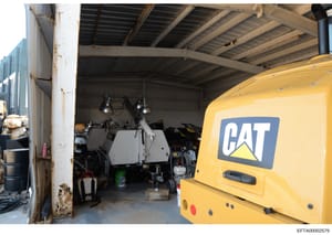 This photograph shows the interior of an industrial or construction equipment storage facility. A yellow Caterpillar (CAT) branded vehicle or equipment is visible on the right side of the image. The facility contains various tools, equipment, and mat