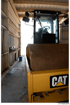 This is a photograph of the interior of an industrial or agricultural storage building, showing a yellow Caterpillar (CAT) forklift vehicle parked inside. The metal-frame building has corrugated metal walls and ceiling with skylights providing natura
