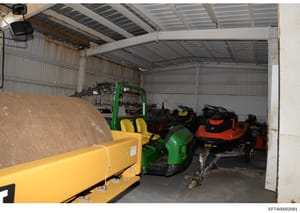 This photograph shows the interior of a large metal warehouse or storage facility containing various industrial equipment including a green and yellow forklift (Terex brand), multiple all-terrain vehicles or small utility vehicles in different colors