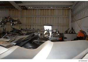 This is a photograph of the interior of a large corrugated metal warehouse or hangar containing multiple jet skis (personal watercraft), storage equipment, and industrial lighting. The space appears to be a recreational facility or storage hangar, wi