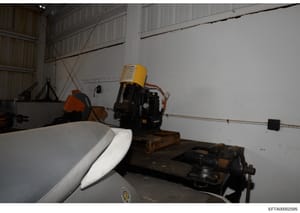 This photograph shows the interior of an aircraft hangar containing various aviation maintenance and support equipment, including what appears to be a work platform or lift with a yellow canister, aircraft parts or components, and industrial machiner