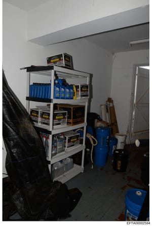 This is a photograph of a storage or utility room containing shelving units stocked with Havoline motor oil products, cleaning supplies, blue containers, and various maintenance equipment. The image appears to be evidence documentation from the Epste