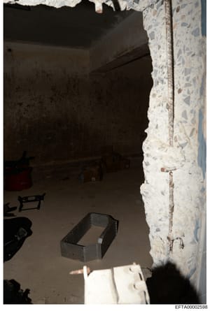 This is an evidence photograph showing an interior room in what appears to be an unfinished or under-renovation state. The image captures a concrete floor, white stone or aggregate wall finish on the right side, dark walls and ceiling, and various co
