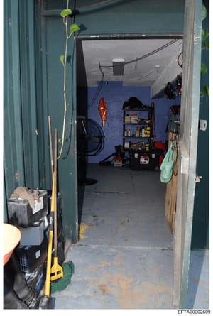 This is a photograph of a storage space or garage interior, showing various tools, equipment, and personal items organized on shelves and the floor. The space has blue flooring, teal/green walls, and contains items such as a red kayak, shelving unit 