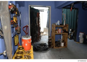 This photograph shows the interior of a blue-painted storage room or utility space containing various construction and maintenance equipment, including rigging gear, electrical cables, safety equipment, and tools. The image appears to be part of evid