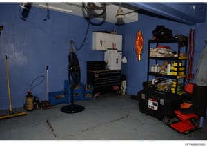 This is an evidence photograph showing the interior of a garage or workshop area with bright blue walls. The space contains various tools, equipment, and storage items including a toolbox, shelving units, sporting equipment (skis visible), and miscel
