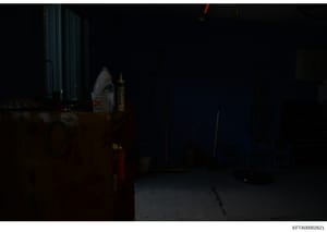 This photograph shows a dimly-lit interior space containing various household items and cleaning supplies, including what appears to be a bleach bottle and other containers. The image quality is poor due to low lighting conditions, making specific de