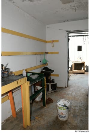 This photograph documents an interior space undergoing construction or renovation, featuring yellow wooden framing on walls, exposed materials, and basic furnishings. The room appears to be in a state of renovation with visible work-in-progress eleme