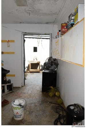 This photograph documents an interior room in what appears to be a property under renovation or construction. The space shows exposed ceiling, damp walls, construction materials, and various equipment scattered throughout, suggesting the room was in 