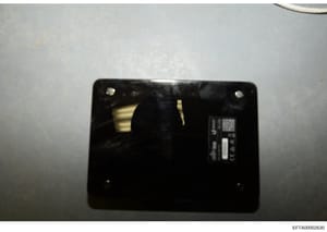 This is a close-up forensic photograph of the interior of an electronic device, showing a black circuit board or component panel with mounting points and what appears to be a manufacturer label or serial number plate on the right side. The image qual