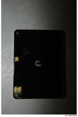 This is a photograph of a black electronic device, likely a computer or laptop, shown from above against a light background. The device displays a logo on its back cover and shows signs of wear and age. This appears to be evidence documentation from 