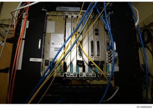 This is a photograph of an interior view of an electrical panel or server rack containing Panasonic equipment, multiple circuit boards, and extensive wiring in blue, yellow, and orange colors. The image appears to be evidence documentation from a pro