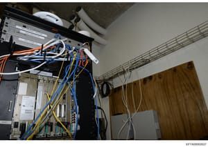 This photograph documents a professional computer server installation and network infrastructure setup, showing mounted APC networking equipment, multiple network switches, and extensive cabling in various colors (orange, blue, yellow, white). The im