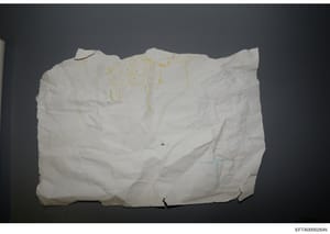 This is a photograph of a hand-drawn sketch or blueprint on aged, creased white paper, appearing to show architectural or property layout designs with yellow and blue markings indicating different sections or areas. The document is worn and wrinkled,
