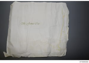 This is a photograph of what appears to be a white linen or paper architectural drawing cover or blueprint folder bearing handwritten text in cursive reading '94 James Gut' in gold or yellow ink. The item shows fold lines and wear consistent with age