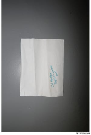 This is a photograph of a folded white paper or envelope with handwritten text in blue ink. The visible text appears to read 'CJ Marachi' and possibly 'Tenerife-1982' or similar, though the handwriting is difficult to read with complete certainty. Th
