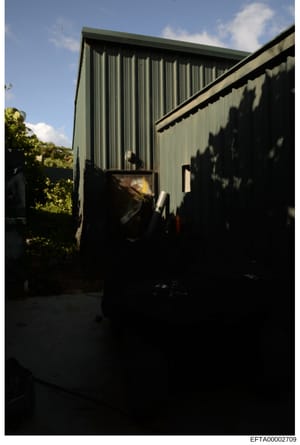 This is a photograph of a large corrugated metal building with a green roof and metal siding. The image shows an exterior view of what appears to be a storage, warehouse, or outbuilding structure, photographed during daytime with clear sky visible. T